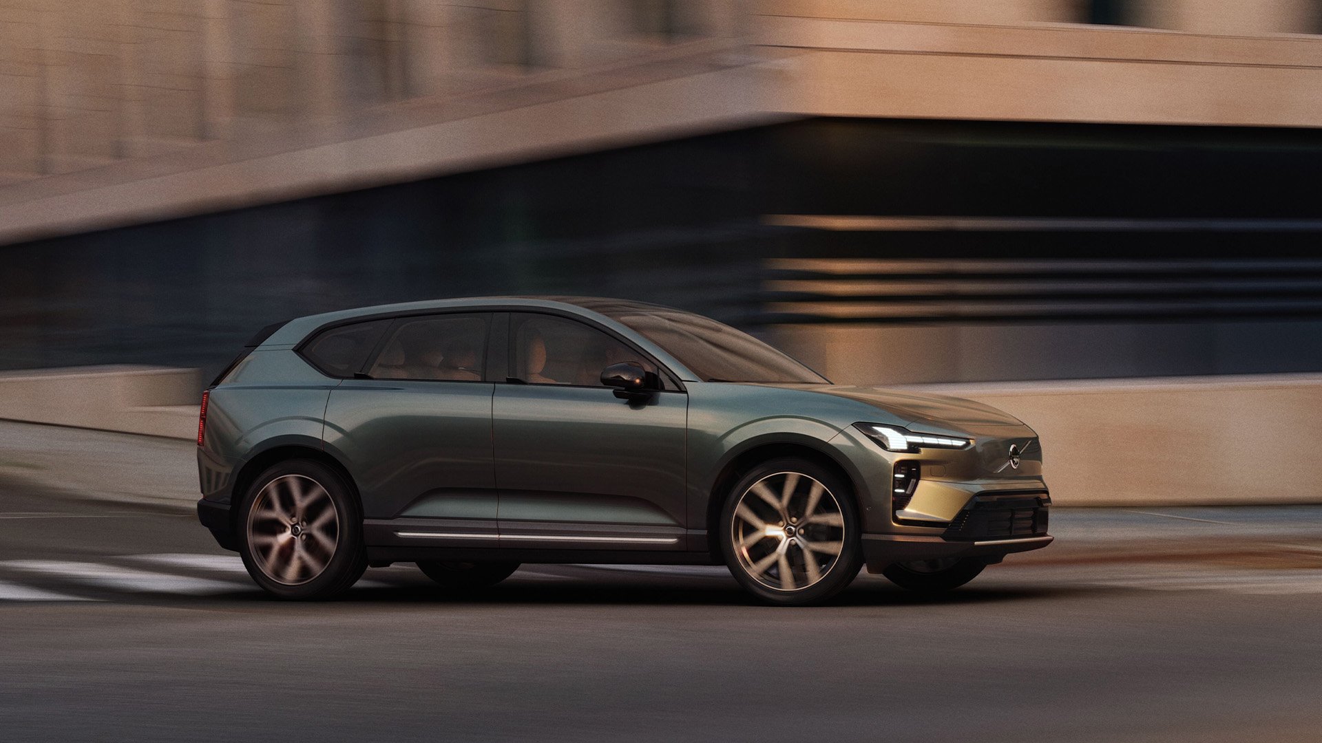 Mörkgrön Volvo EX60 i profil i urban miljö.