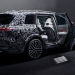 Kamouflerad Audi Q9 med bakdörren öppen i studiomiljö.