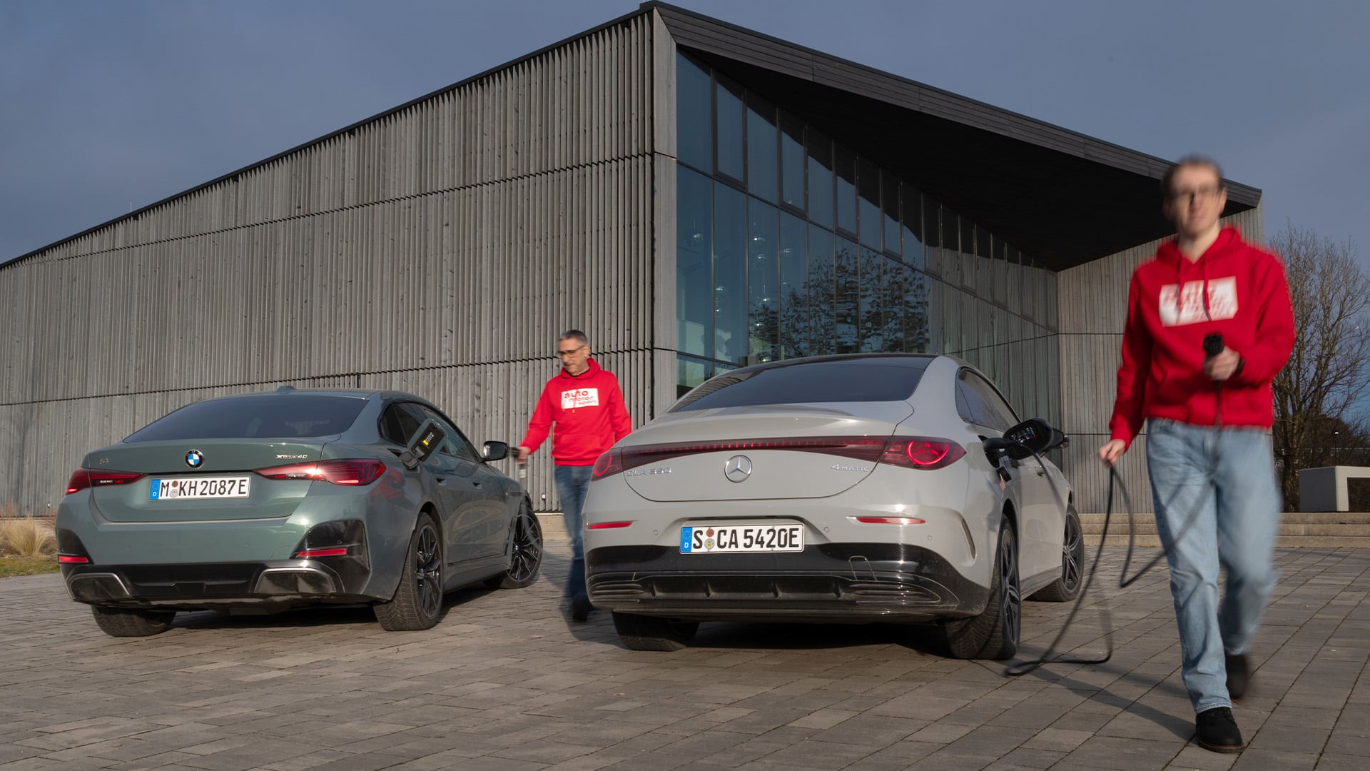 BMW i4 och Mercedes CLA parkerade med två redaktörer från auto motor und sport i bild.