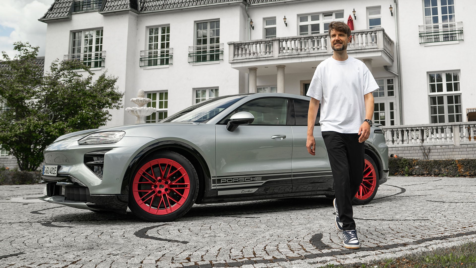 John Sempill framför en Porsche Cayenne Coupé Electric i silver med röda fälgar.
