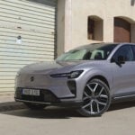 En Volvo EX60 i Aurora Silver parkerad framför en sandig husfasad.