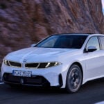 Vit BMW i3 kör på en bergsväg med hav i bakgrunden.