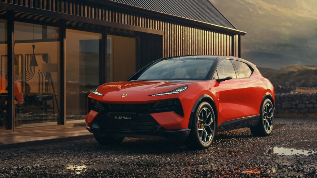 Röd Lotus Eletre X snett framifrån med stuga och berg i bakgrunden.