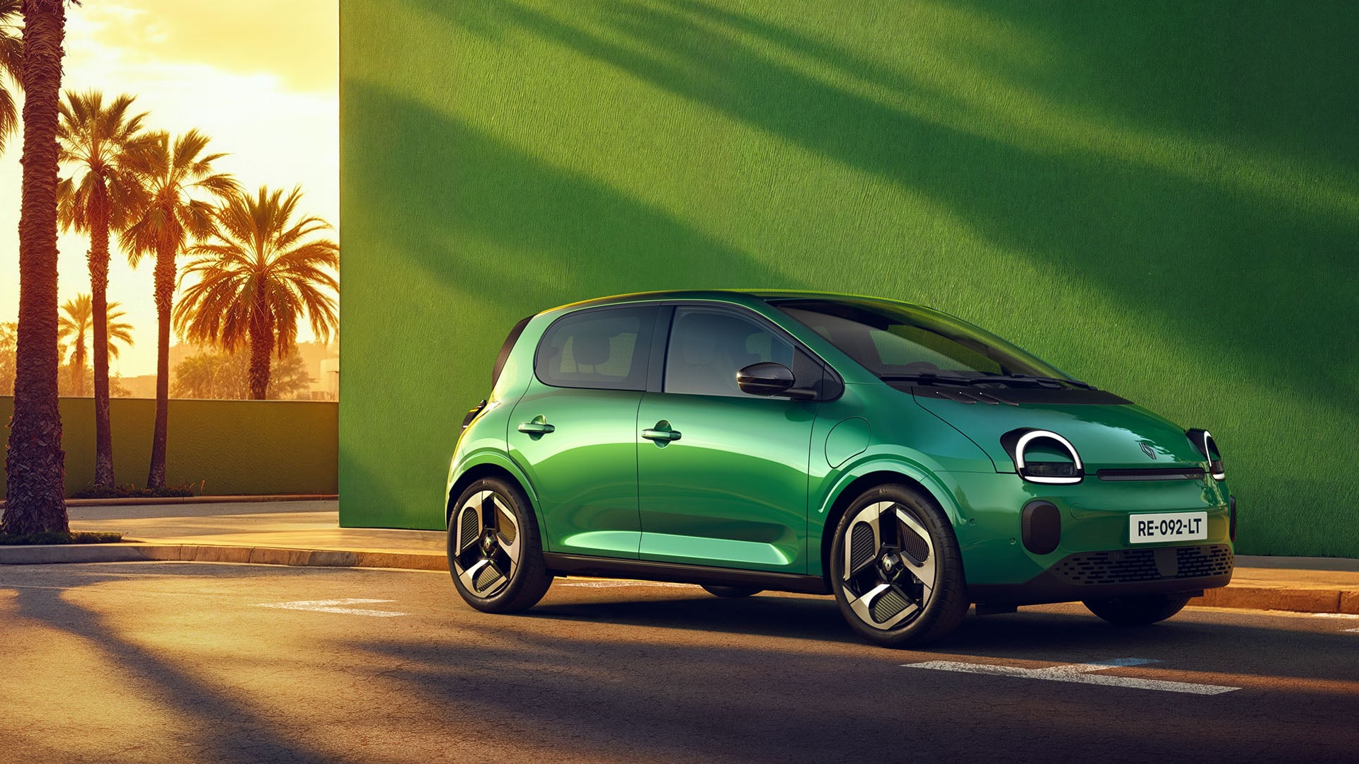 Grön Renault Twingo E-Tech i profil i solnedgången mot en grön fasad.