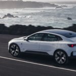 Vit Polestar 4 på snett bakifrån på strandväg med hav i bakgrunden.
