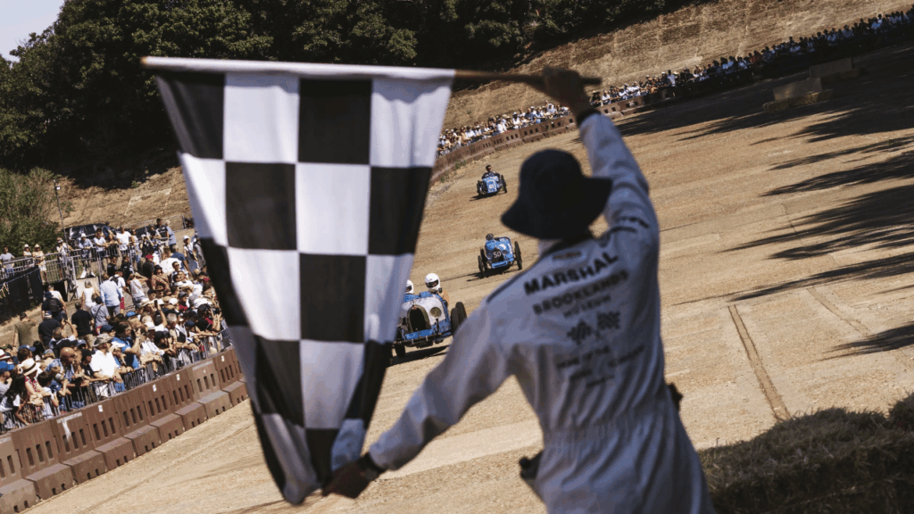 Den målflaggade målflaggan viftas över de klassiska racerbilar som körde demorundor på de bevarade, doserade betongpartierna av den historiska banan. Foto: Brooklands Museum