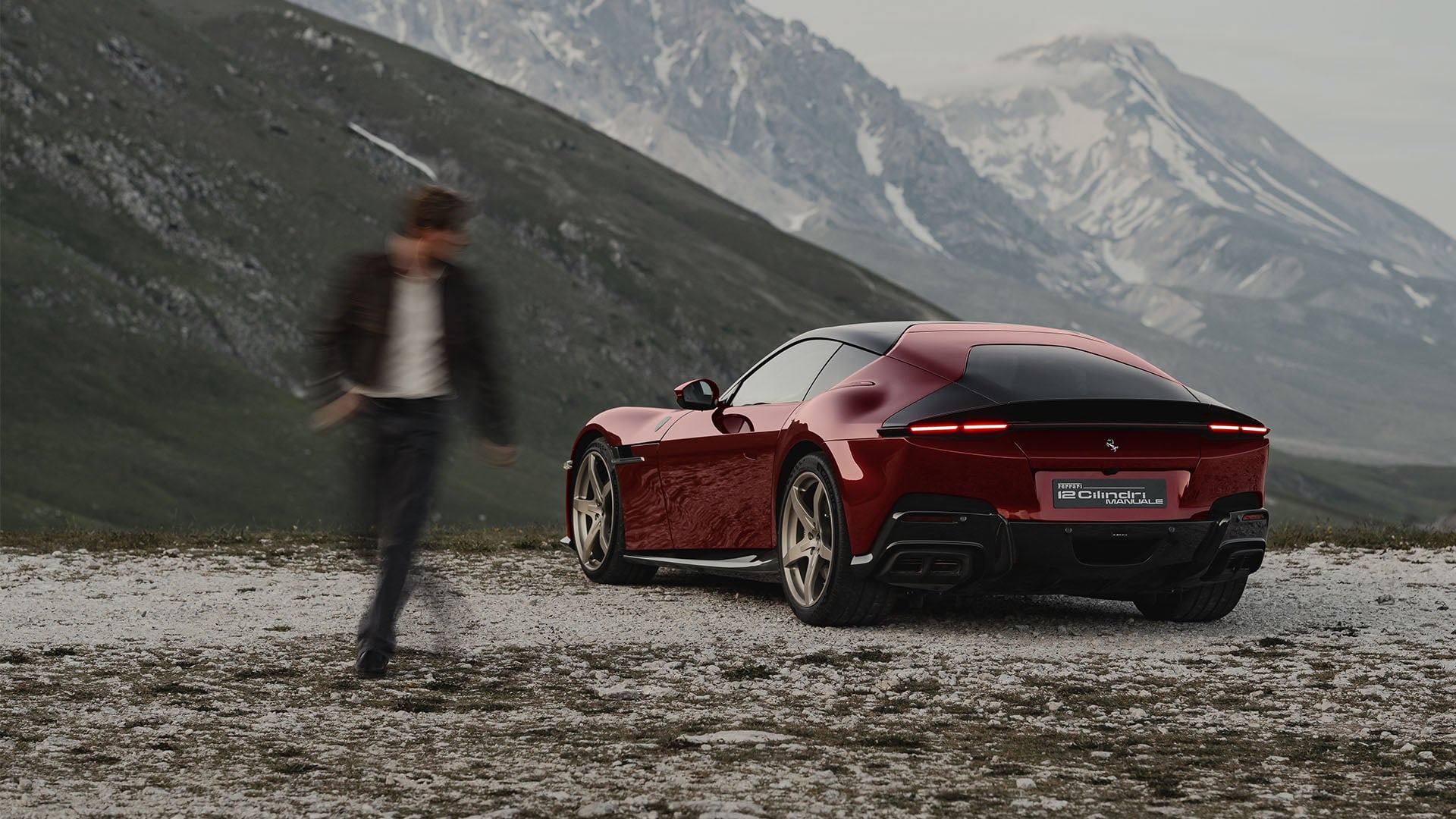 Ferrari 12Cilindri Manuale parkerad med berg i bakgrunden och en människa ur fokus som tittar på den.