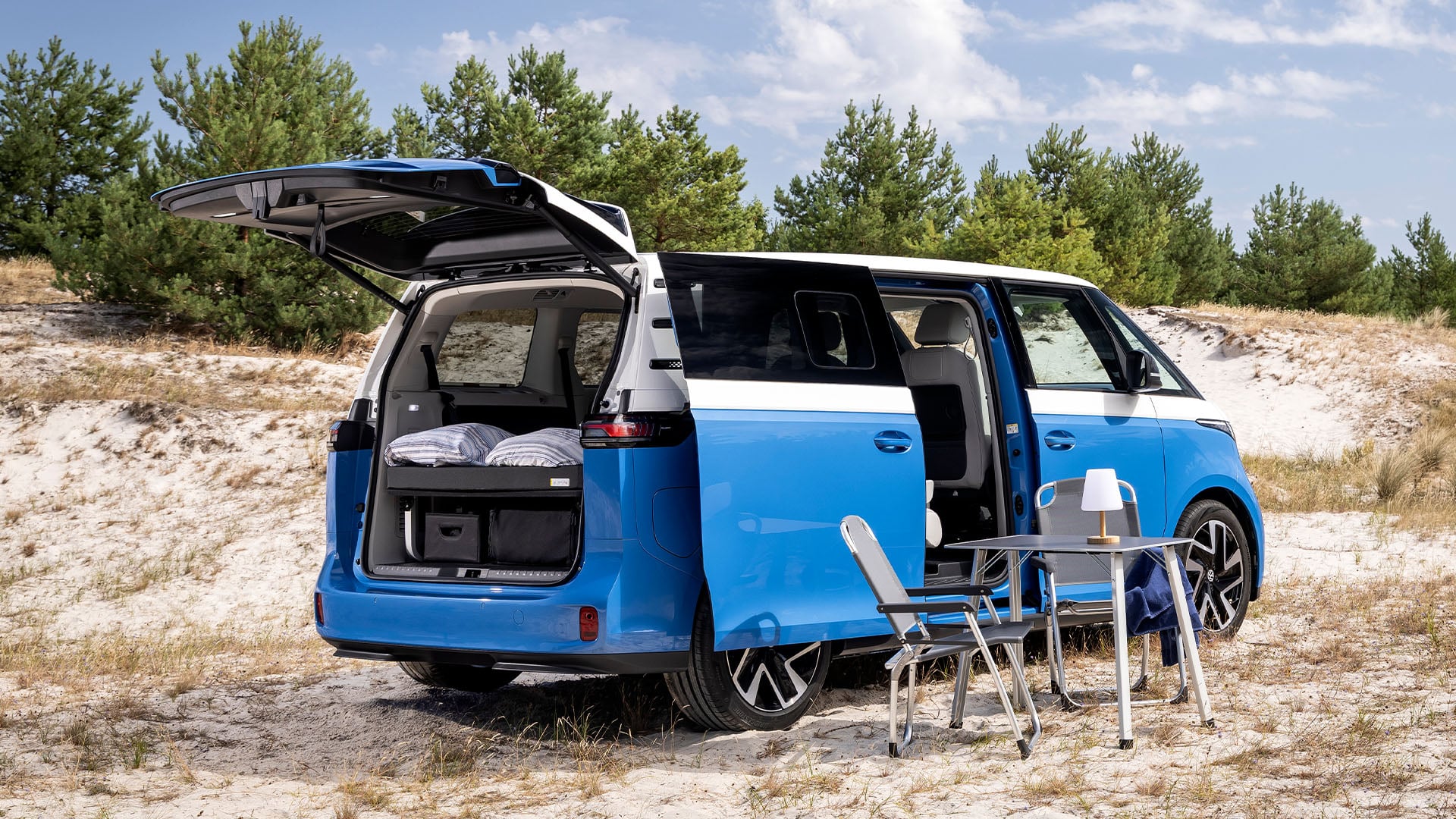 Blå Volkswagen ID. California Cruise parkerad med campingbord uppställt.
