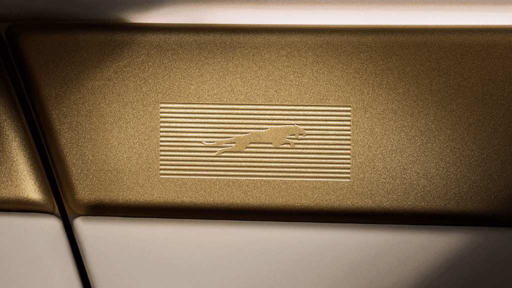 Subtila detaljer i varm mässingston smyckas av Jaguars klassiska ”Leaper”, invävd mot en räfflad struktur. Materialvalen är inspirerade av travertinsten och hantverksmässiga textilier för en retrofuturistisk känsla. Foto: Jaguar