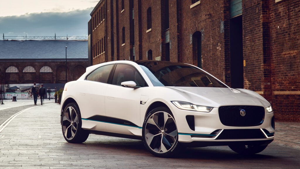 Vit Jaguar I-Pace snett framifrån parkerade med en tegelfasad i bakgrunden.