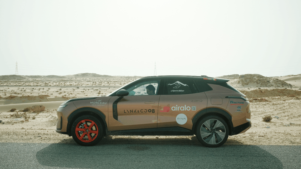Profilvy av Lynk & Co 08 med sina distinkta orangea hjulnav och sponsordekaler mot det karga ökenlandskapet. Foto: Lynk & Co