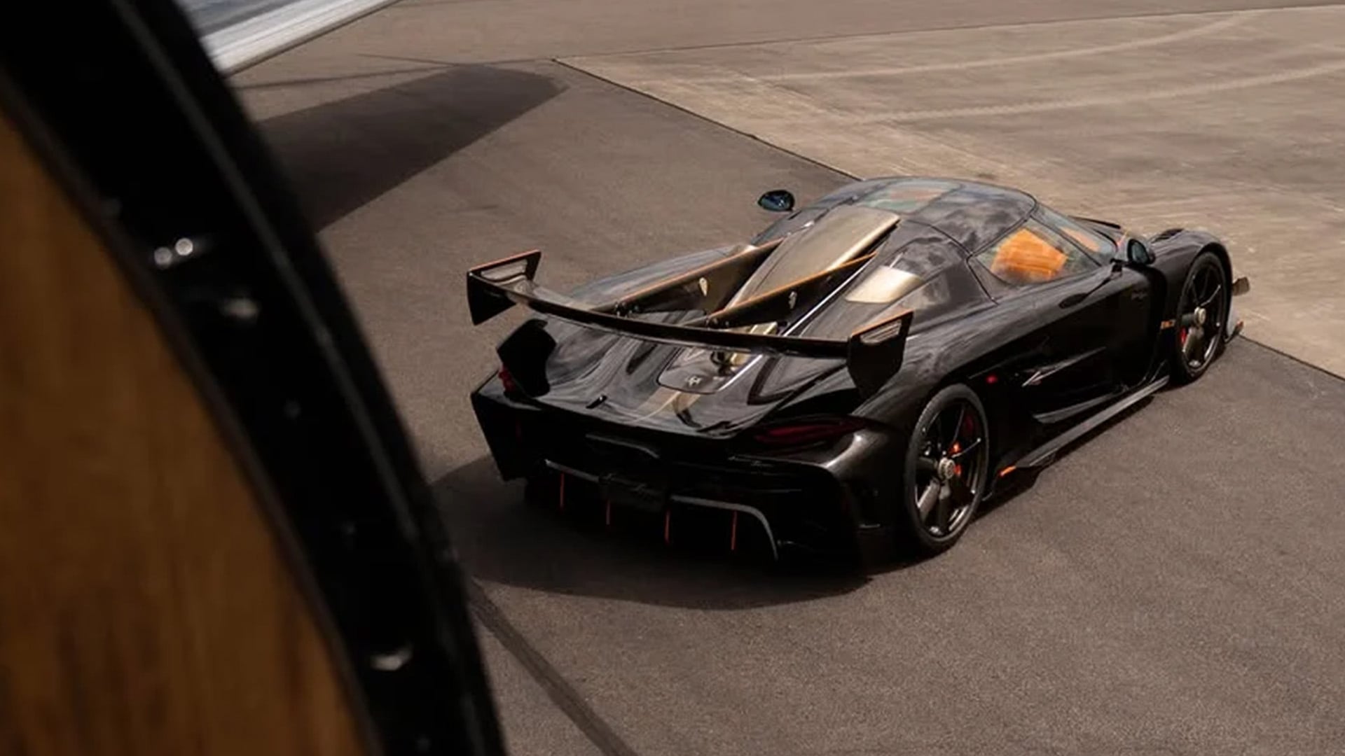 Svart Koenigsegg Jesko Sadair’s Spear bakifrån i hög vinkel på startbana under en flygplansvinge.