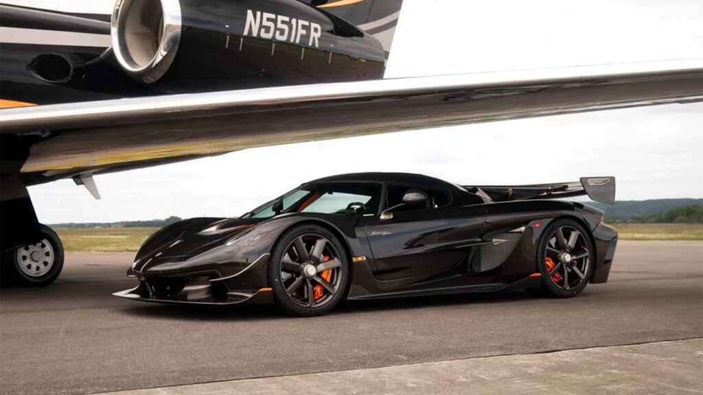 Svart Koenigsegg Jesko Sadair’s Spear från sidan på startbana under en flygplansvinge.