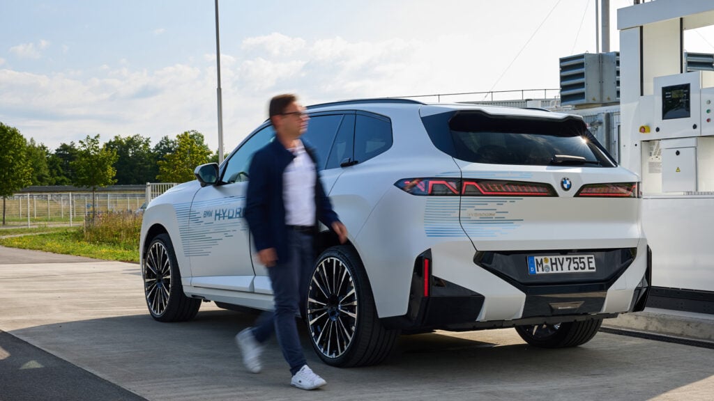 Vit BMW iX5 Hydrogen vid tankstation men en person vid bilen.