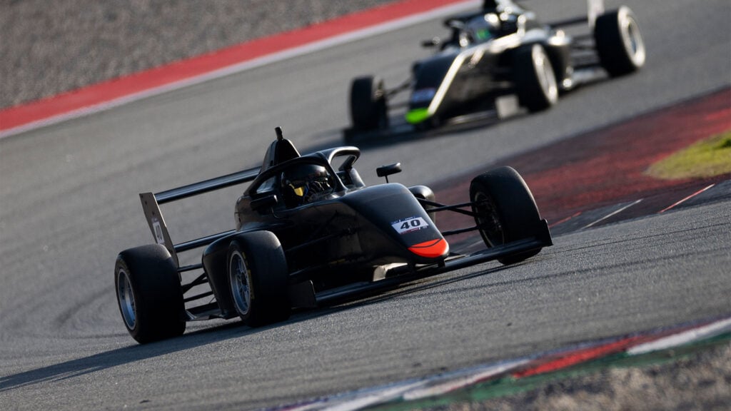 Två Formel 4 CEZ-racingbilar kör snabbt genom en kurva på en racerbana.