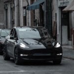 Svart Tesla Model Y i trafik i ett område med tegelbyggnader.