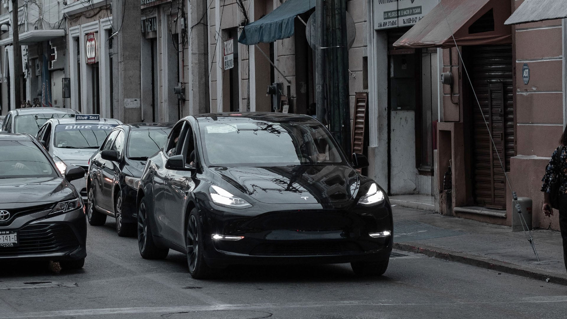 Svart Tesla Model Y i trafik i ett område med tegelbyggnader.