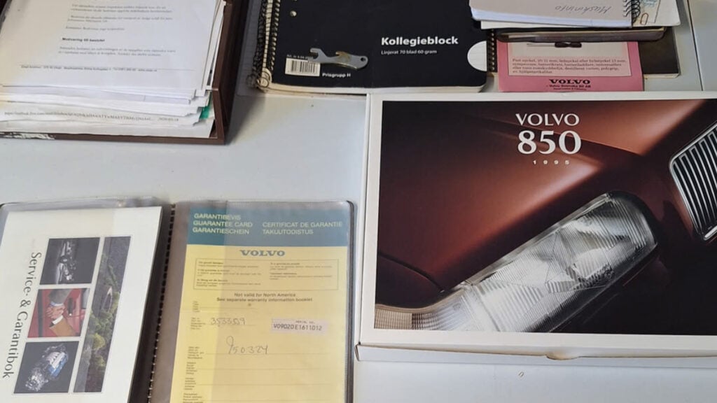Tillbehör och instruktionsböcker till en blå Volvo 850 med 27 mil på mätaren.