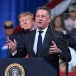 Audi-chefen Gernot Döllner talar vid en talarstol på Donald Trumps valmöte i Georgia, med Trump stående bakom honom.