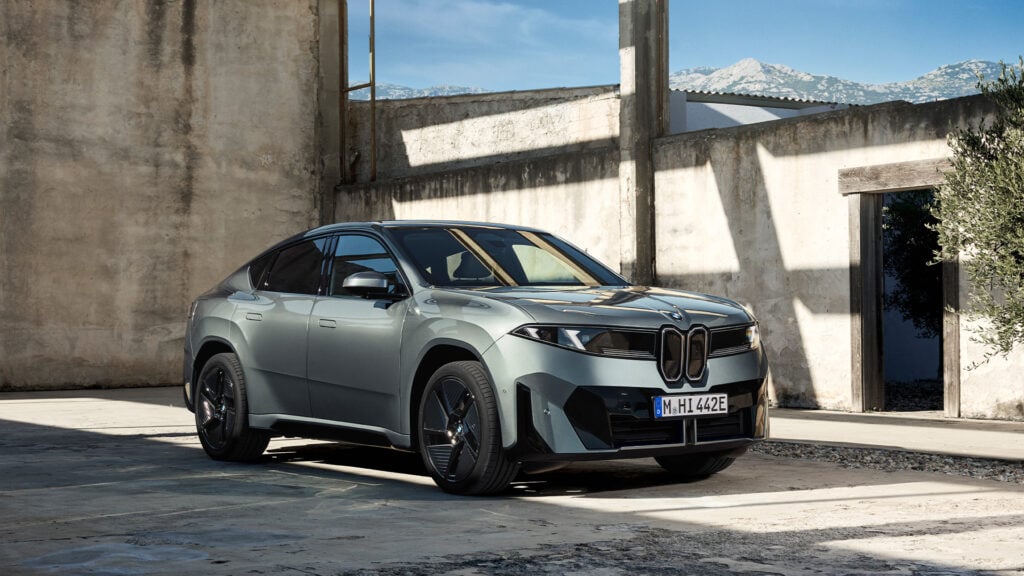 Grå BMW iX4 Neue Klasse snett från sidan mot urban miljö.