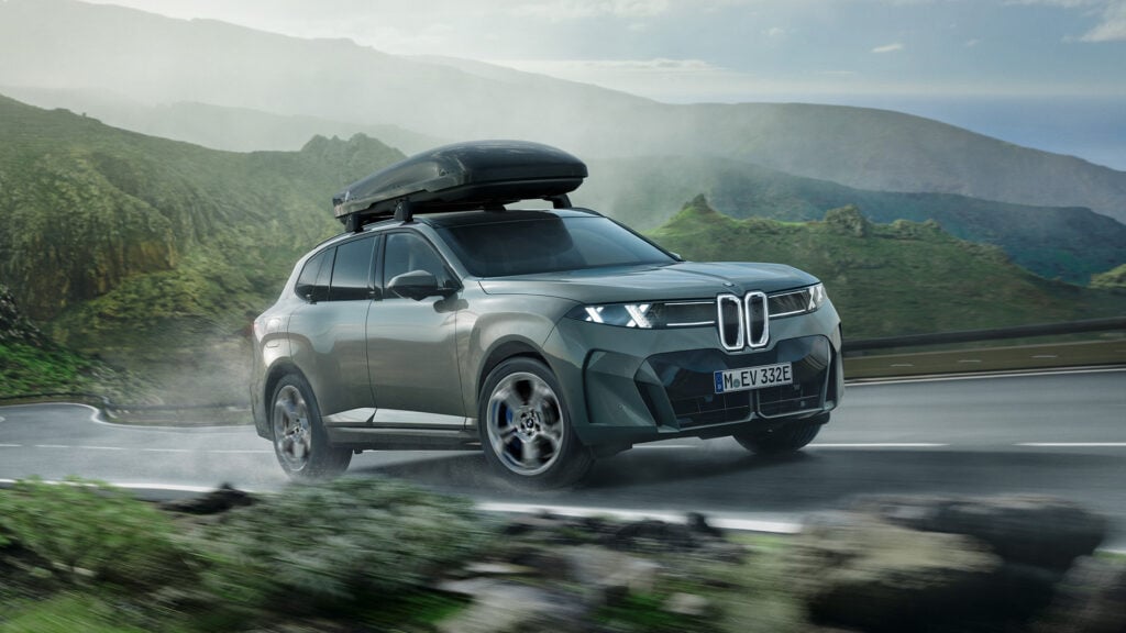 Grön BMW iX5 snett framifrån med takbox i naturen.