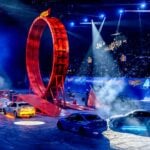Hot Wheels-stuntshow i arena med flera bilar, rök, publik och en stor loop på banan.