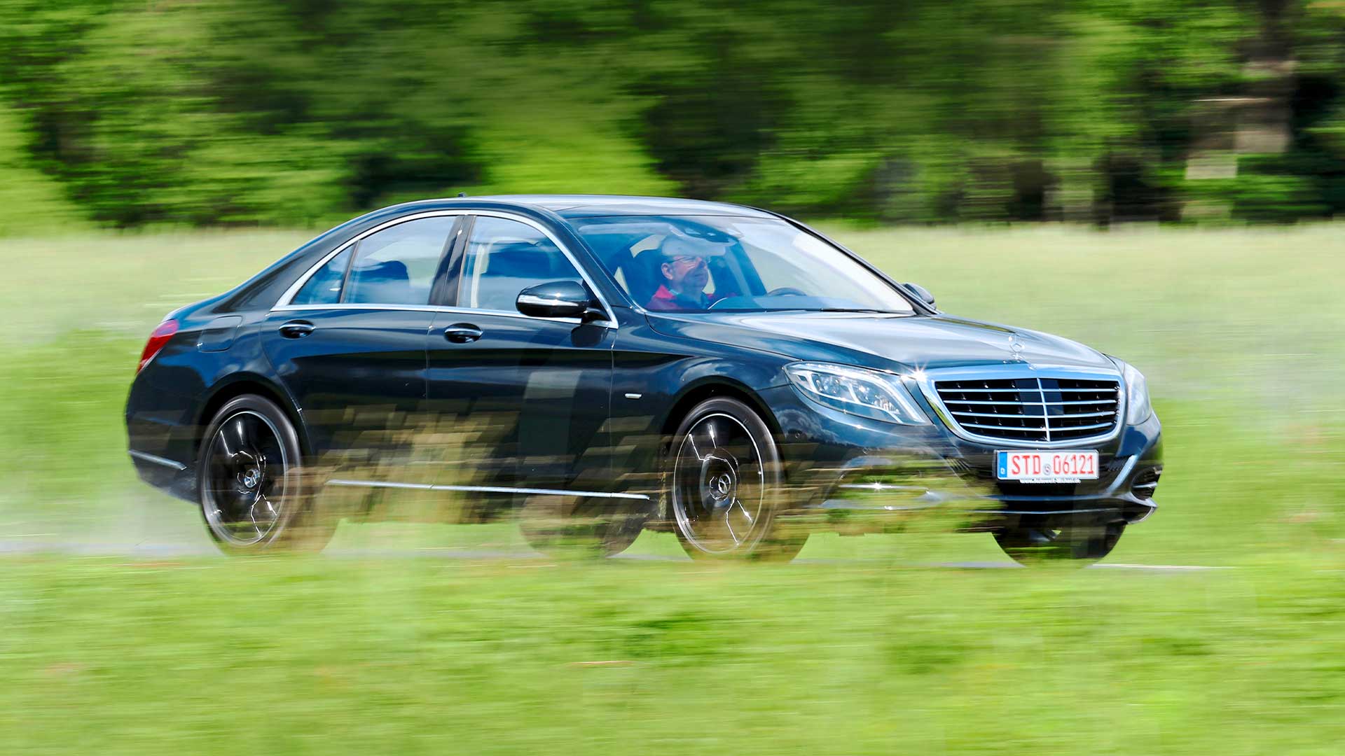 Svart Mercedes S-klass körandes på väg med gröna fält omkring.