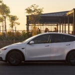 Vit Tesla Model Y i profil med solnedgång i bakgrunden.