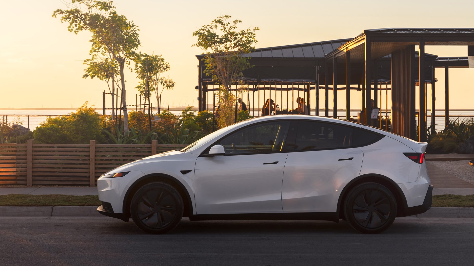 Vit Tesla Model Y i profil med solnedgång i bakgrunden.